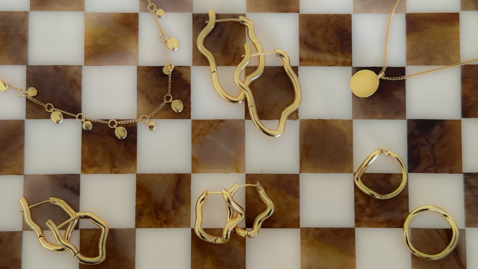 Gold jewelry including rings and a necklace on a checkered surface